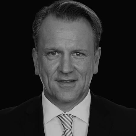 Schwarz-Weiß Portrait von Herrn Müller in Anzug und gestreifter Krawatte. Er lächelt in die Kamera.