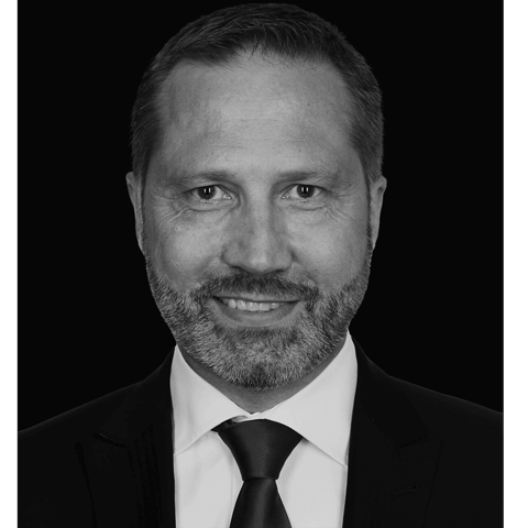 Schwarz-Weiß Portrait von Herrn Nagl in Anzug und Krawatte. Er lächelt in die Kamera.